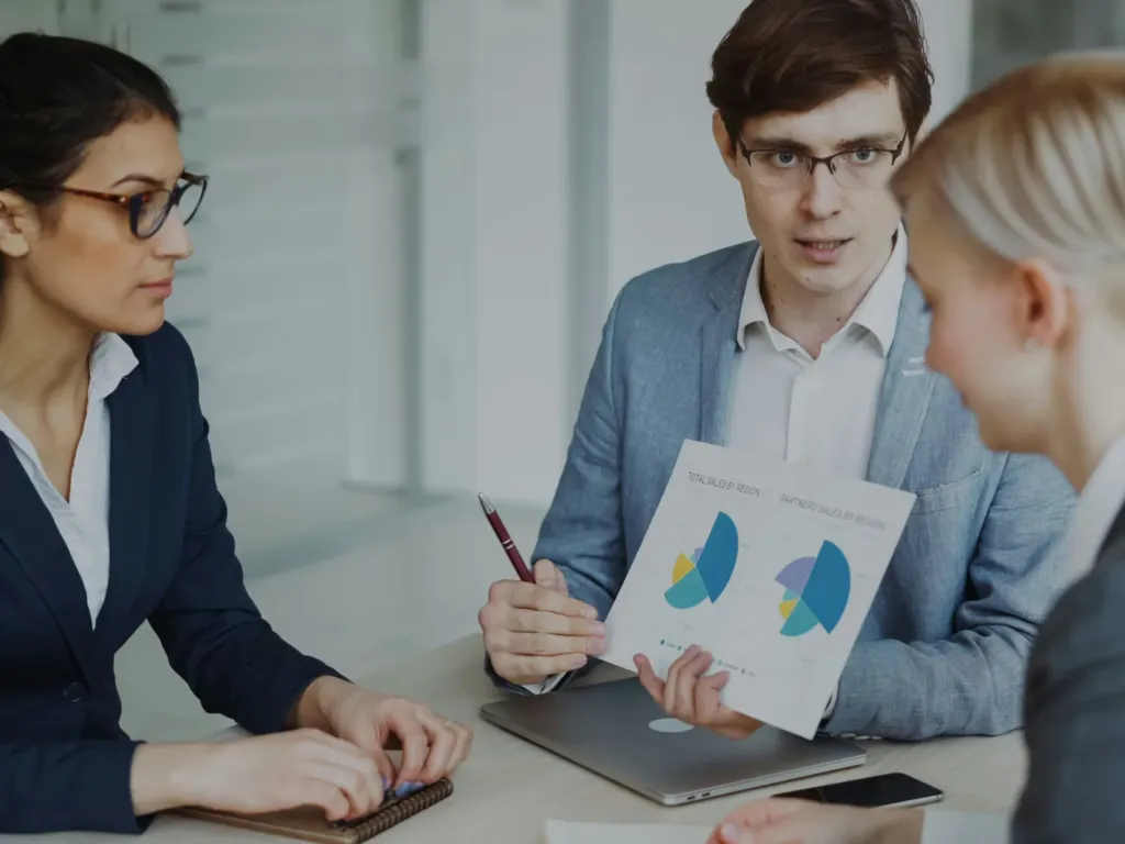 Three colleagues at a meeting table reviewing a printed chart