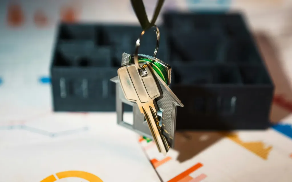 Keys on a house-shaped key ring above printed charts and a model house