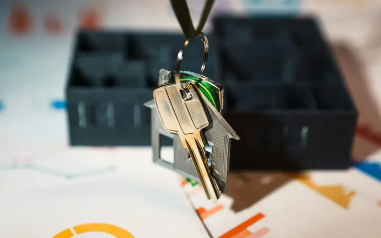 Keys on a house-shaped key ring above printed charts and a model house