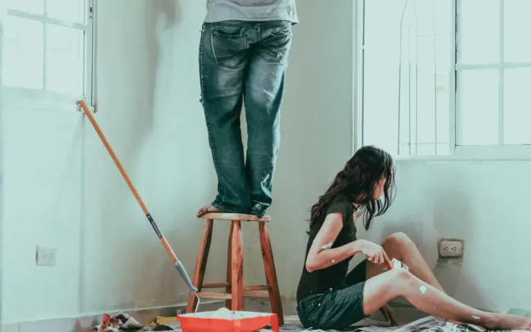 Two people painting the walls of a bright room